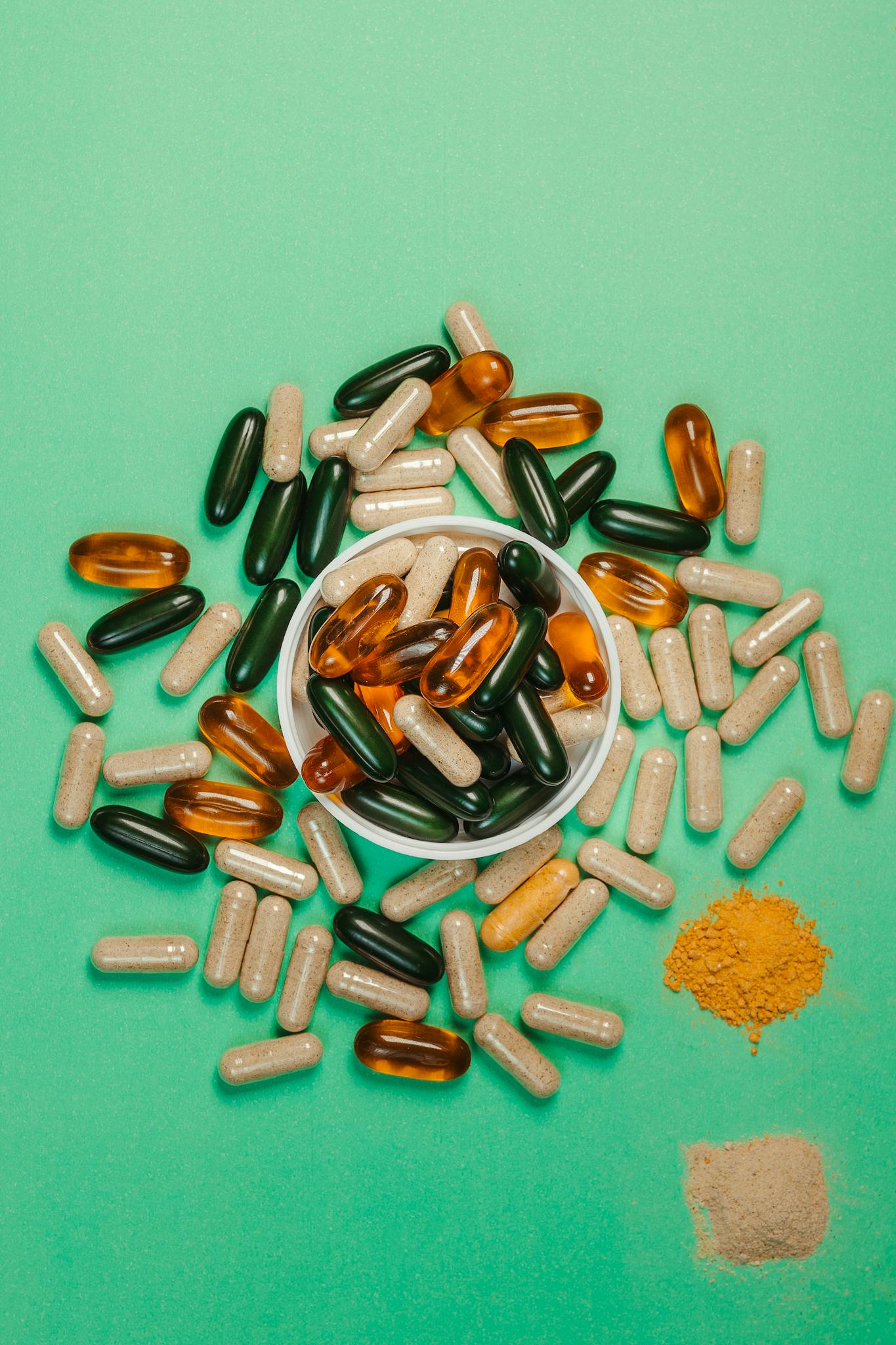 An assortment of capsules and powders on a green backdrop, symbolizing health and wellness.