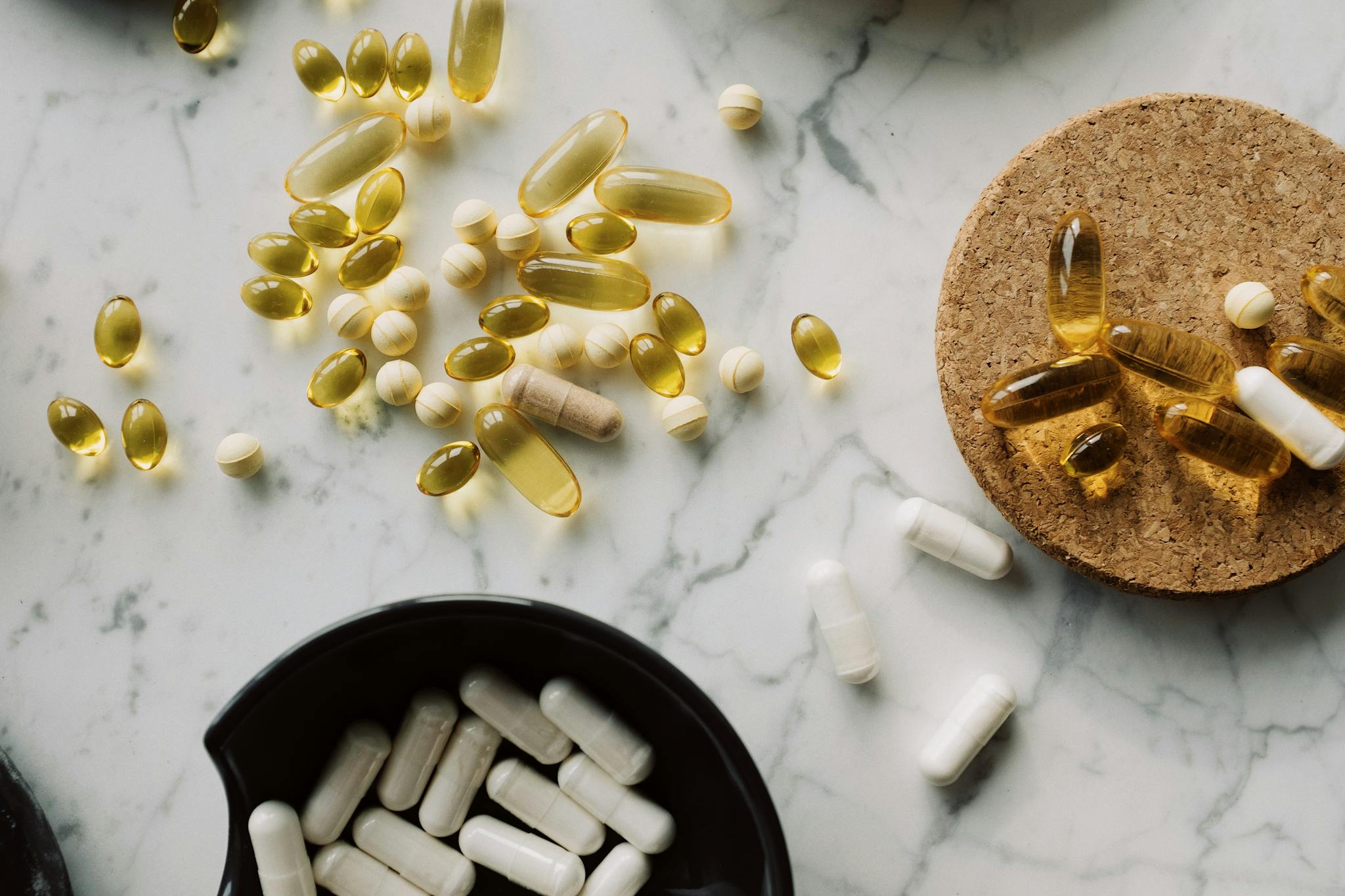 From above of mixed white vitamins and omega placed in black bowl on cellulose stand and scattered around the table